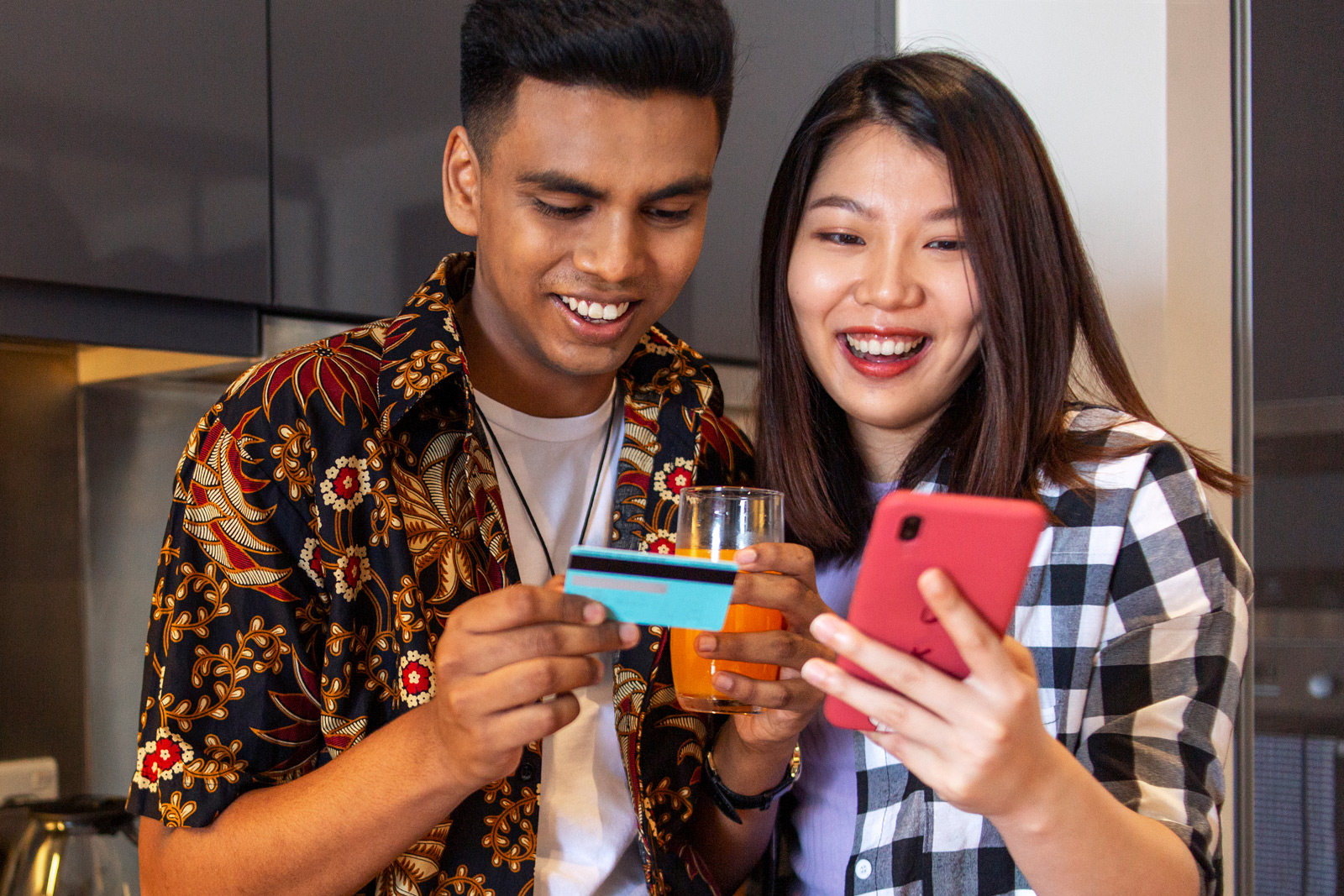 A man and a woman smile while making credit card purchases on a smartphone.
